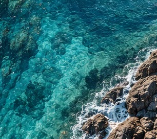 Aerial view of turquoise water breaking over dark rocks